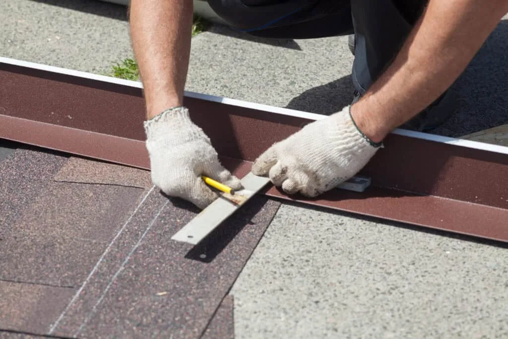 Two gloved hands positioning a shingle with a measuring tool